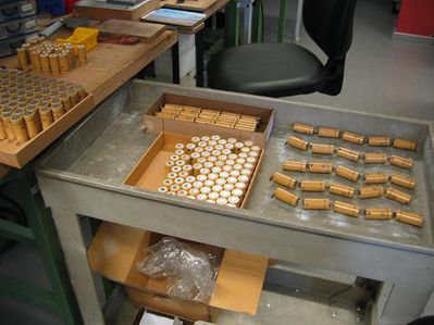 lose Stränge
In der Mitte des Rolltisches die Zellen auf der Lieferpalette, rechts davon lose 5er Stränge, links auf dem Tisch bereits mit einer Lötfahne vorbereitete Zellen auf Palette.
